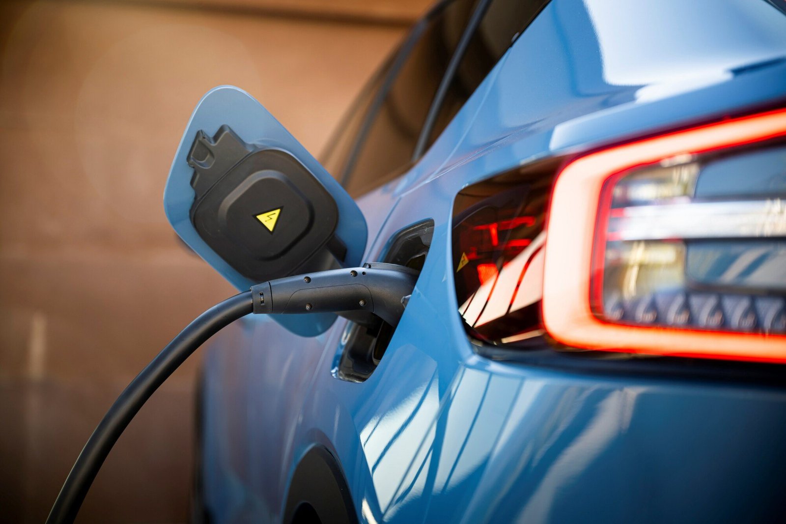 A blue car from behind plugged into a charging plug.