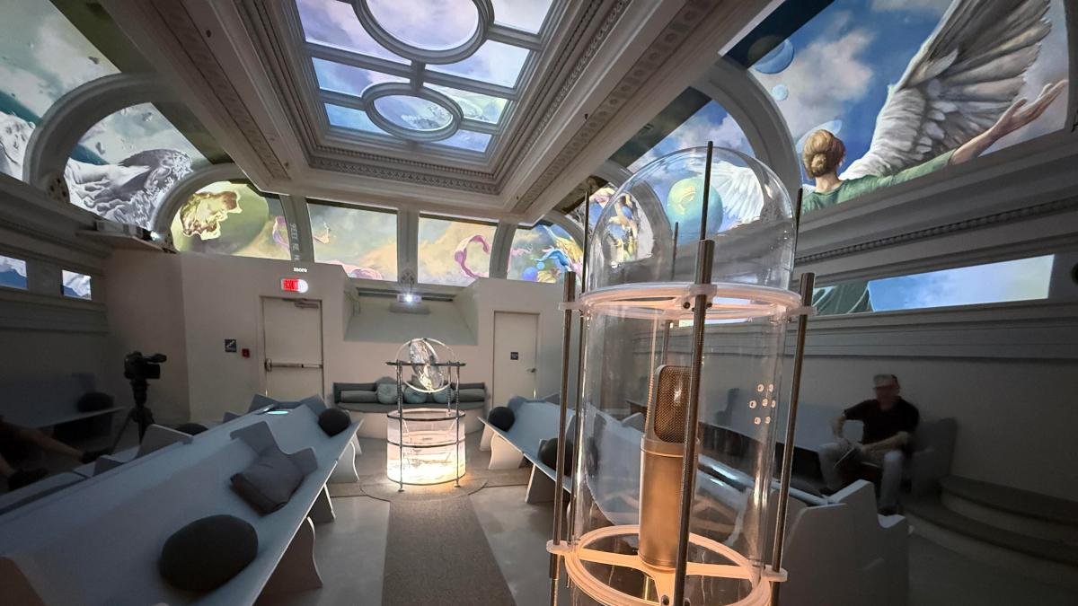 A room with glowing ceiling murals, white chairs and instruments, including a microphone in a glass container.
