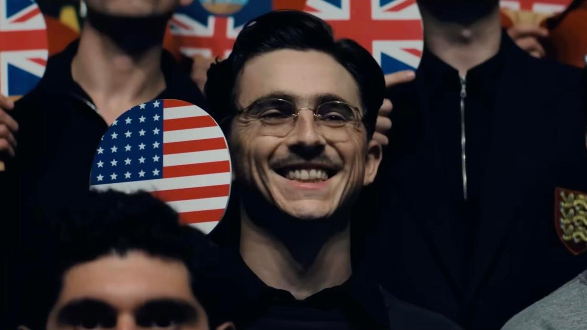 actor Timothée Chalamet smiles and holds a ping pong paddle in the film Marty Supreme
